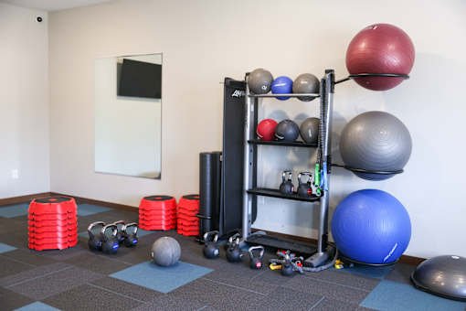 A gym with a variety of equipment including kettlebells, balls, and weight plates.