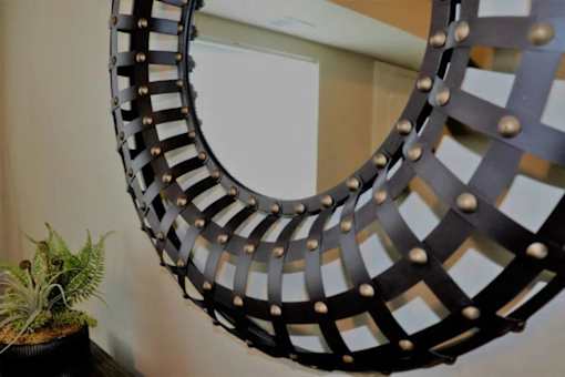A large mirror with a black frame and gold studs is hanging on a wall.