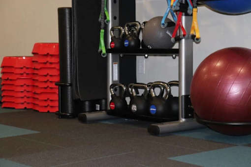 A red exercise ball is on the floor next to a rack of kettlebells.