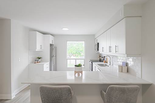A kitchen with a white countertop and two grey chairs.