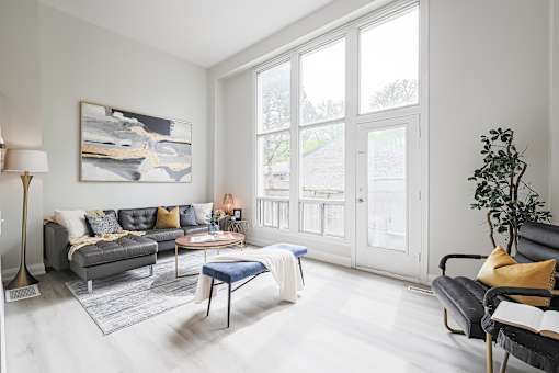 A living room with a grey couch, a blue ottoman, a coffee table, a lamp, a painting, and a potted plant.
