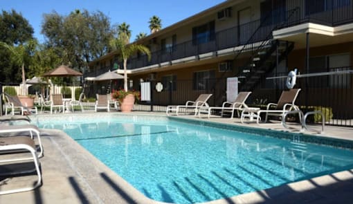 A swimming pool with sun loungers and a building in the background.