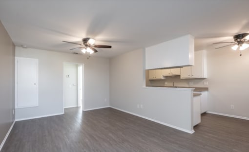 A spacious room with a kitchenette and two ceiling fans.