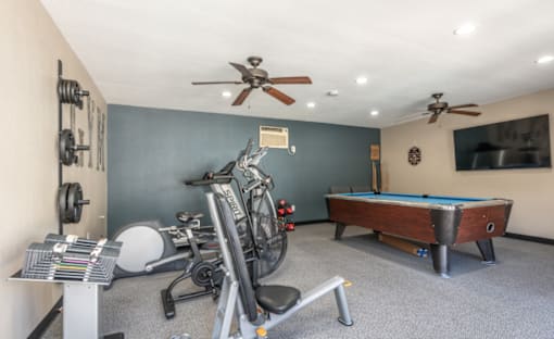 A room with a pool table, exercise equipment, and a fan.