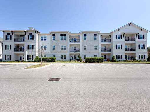 A large white apartment building with a parking lot in front.