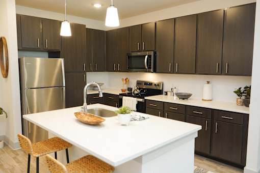 A modern kitchen with a white island and dark brown cabinets.