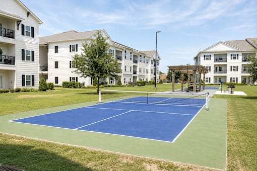 A tennis court is surrounded by apartment buildings.