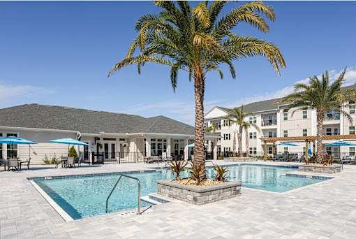 A palm tree stands in front of a pool and apartment building.