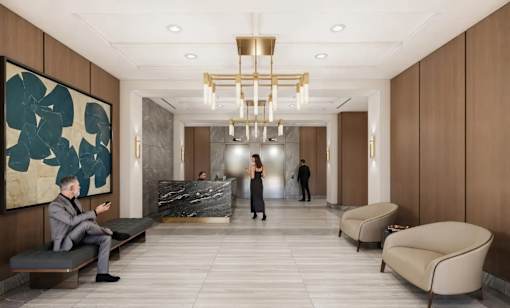 A man in a suit is sitting on a bench in a lobby with a woman standing in the background.