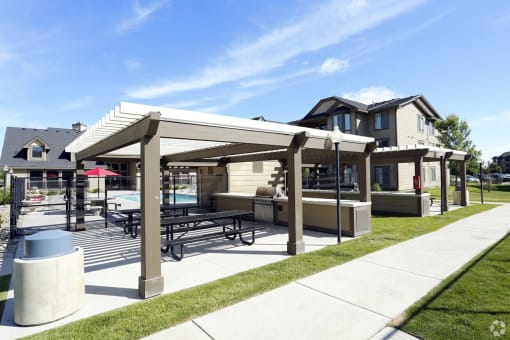 a patio with a picnic table and a grill in front of a house with a swimming pool