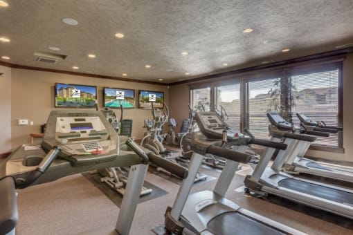 A gym with cardio equipment and three televisions