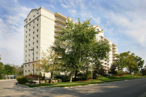 a view from the street of an apartment building with trees and grass in front of it