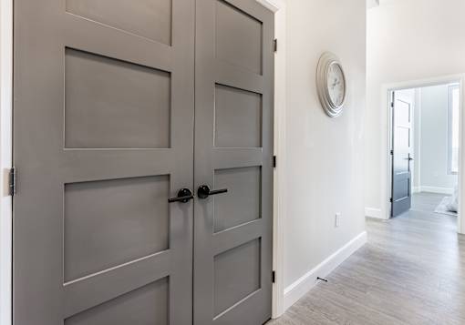 A grey double door with a black handle and a round clock on the wall.