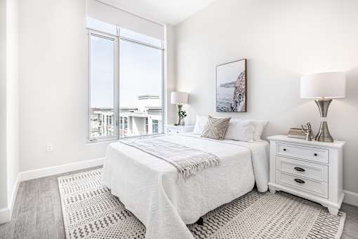A bedroom with a large bed, a nightstand, and a window overlooking a cityscape.