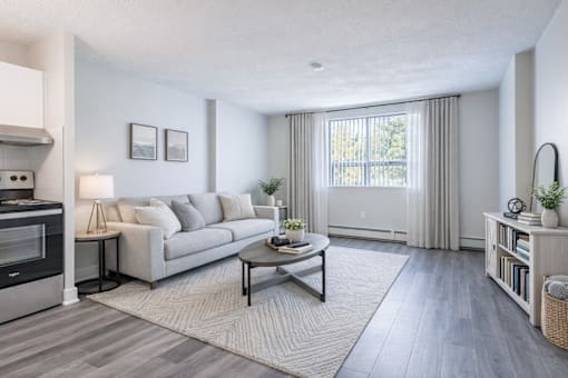 A modern living room with a grey couch, a coffee table, and a large window with curtains.