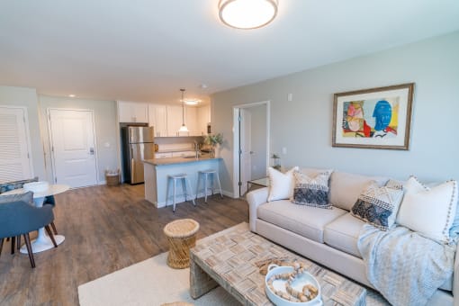 a living room with a couch a table and a chair and a kitchen with a refrigerator and