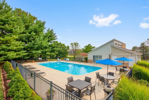 A pool surrounded by a fence and chairs with a house in the background.
