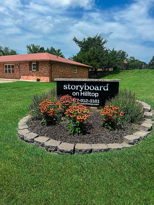 A sign for Storyboard on Hilltop stands in a flowerbed.