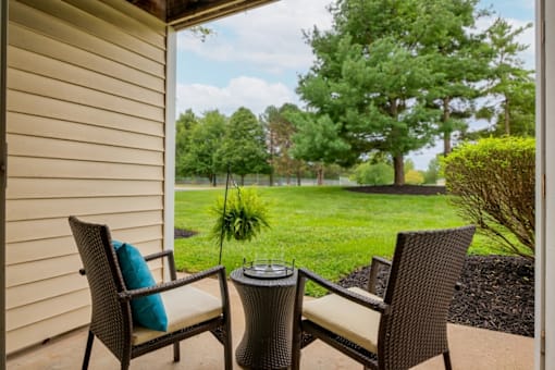 A patio with two chairs and a table with a plant in the background.