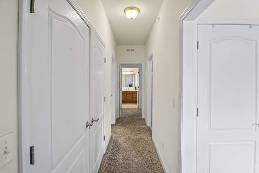 a corridor with white doors and a carpeted floor and a hallway with a bathroom