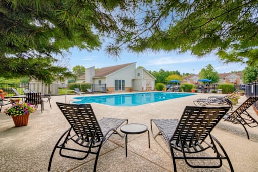 A pool surrounded by chairs and trees with a house in the background.