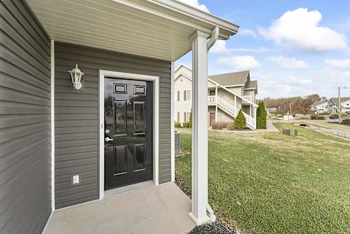 the front door of a home with a lawn and houses in the background