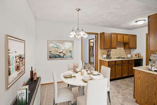 A dining room with a table set for two and a kitchen area in the background.