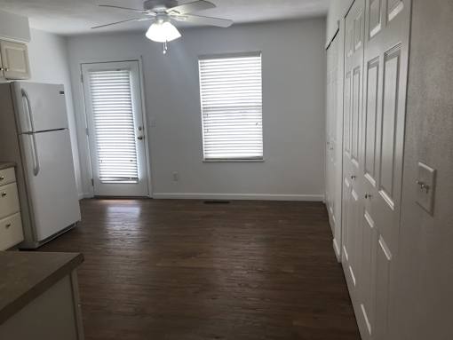 A kitchen with a refrigerator, wooden floors, and white walls.