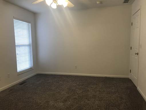 A room with a carpeted floor, a ceiling fan, and a window with blinds.