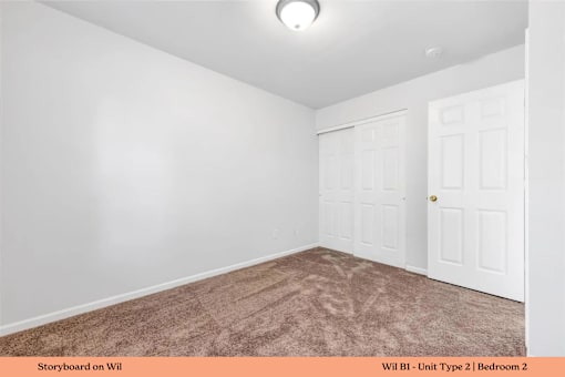 A bedroom with a carpeted floor and two doors.