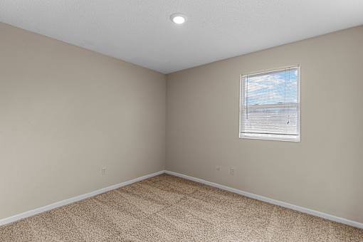 A room with a carpeted floor and a window with blinds.