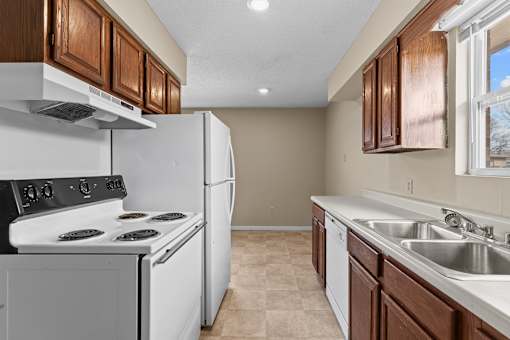 A kitchen with a white stove and refrigerator, brown cabinets, and a tiled floor.