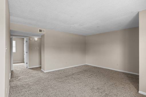 A large, empty room with carpeted flooring and a doorway leading to another room.