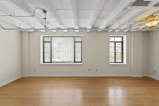 an empty room with two windows and a wood floor
