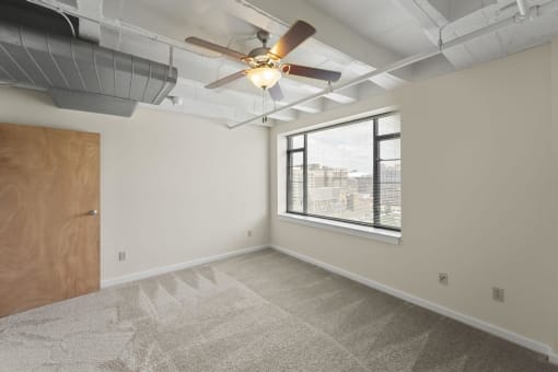 an empty room with a large window and a ceiling fan