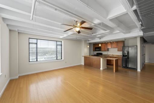 an empty living room with a kitchen and a ceiling fan