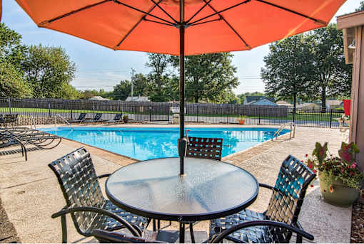 A table with chairs and an umbrella is set up by a pool.