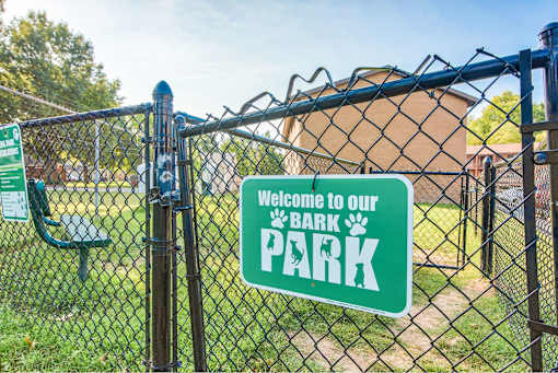 A green sign on a fence reads "Welcome to our BARK PARK".