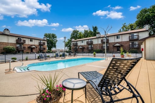 A pool area with chairs and a table in front of apartment buildings.
