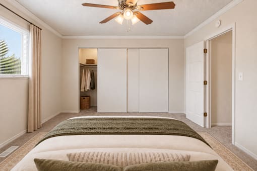 A bedroom with a bed, a ceiling fan, and a closet.
