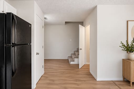 A black fridge is in a white room with a wooden floor.