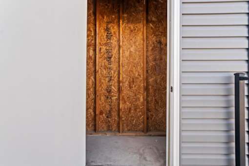 A wooden door with a white wall on the left and a white wall with a black railing on the right.