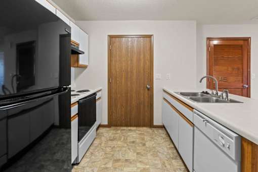 A kitchen with a black refrigerator, white cabinets, and a wooden door.