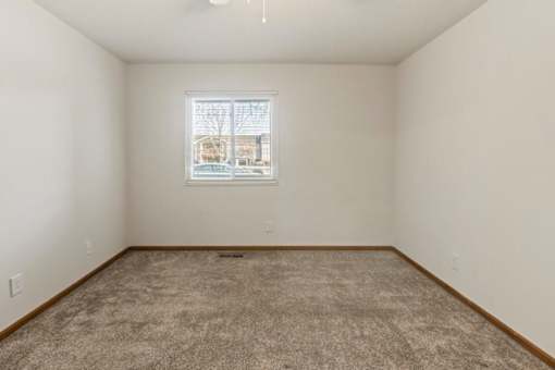 A room with a carpeted floor and a window showing a view of a house.