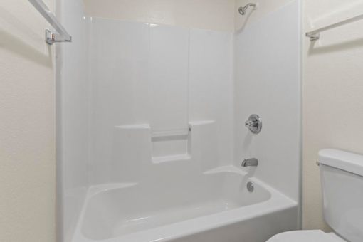 A white bathtub with a shower head and a toilet in a bathroom.