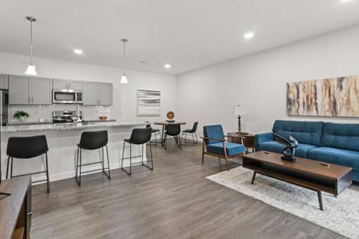 A modern living room with a kitchen area in the background.