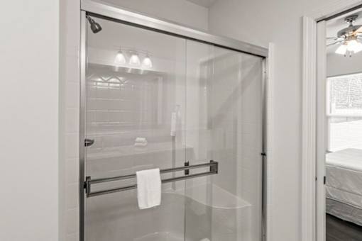 A white bathroom with a glass shower door and a towel hanging on a bar.