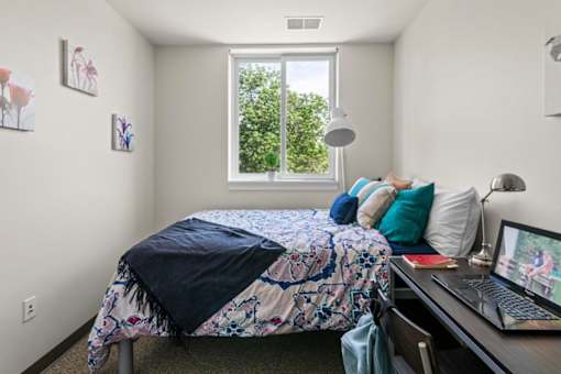 A bedroom with a bed, desk, and laptop.