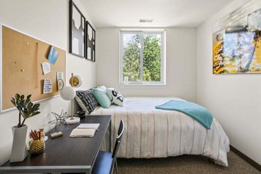 A bedroom with a bed, desk, and window.