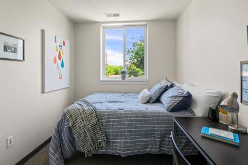 A bedroom with a bed, desk, and window.